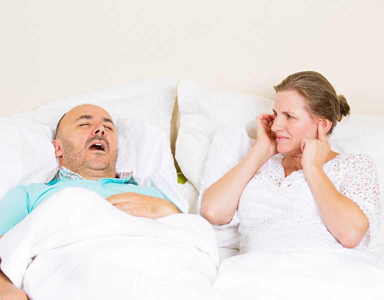 Snoring man sleeping beside an upset woman covering her ears in Stafford, VA