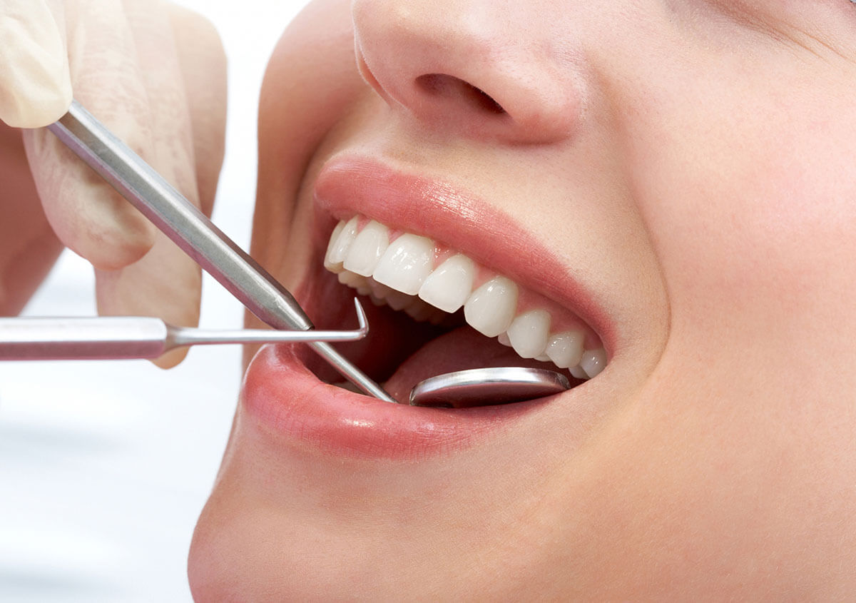 Dental professional examining patient’s teeth with mirror and explorer, illustrating biological dentist approach to dental cavitations in Stafford, VA